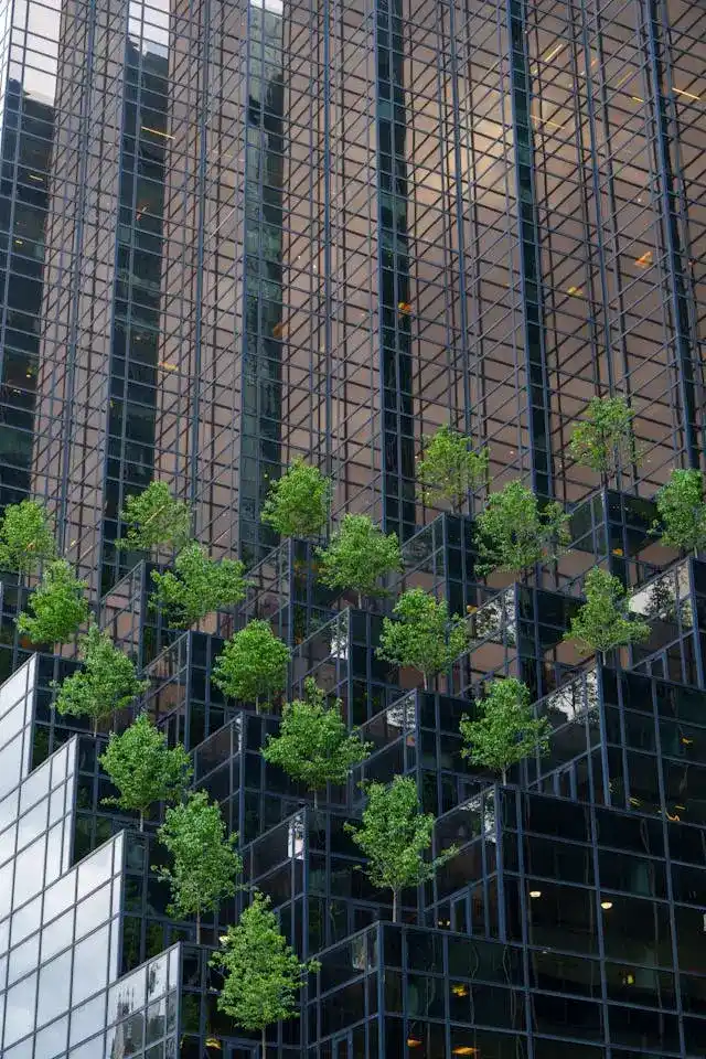 The Regulatory Landscape - A modern glass office building shot from ground level looking up, with green plants or trees visible in the foreground or reflected in the glass facade. The building should appear corporate and sophisticated, ideally with some greenery integrated into the architecture.